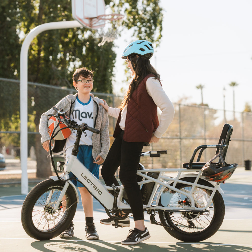 Mom talking to son on basketball court riding XPedition cargo bike with plus 1 seat and barrow bar installed